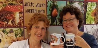 Ineke Kappé en Jacqueline van Wanrooij staan met fotomokken bij een XL-print