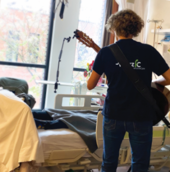 Foto van een muzikante met een gitaar, die voor een patiënt speelt