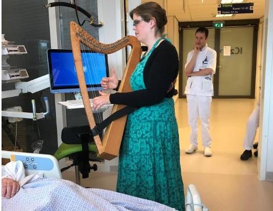 Foto van een muzikante met een harp, die voor een patiënt speelt