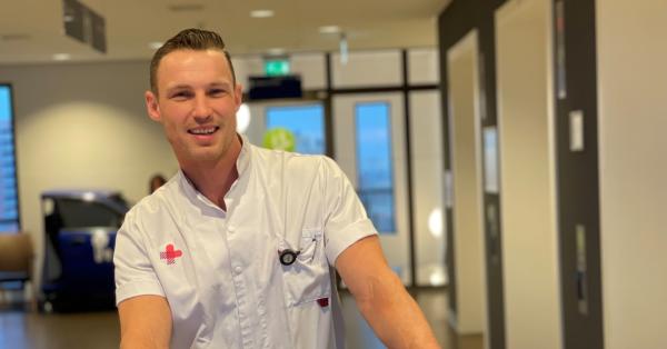 Man in JBZ werkkleding staat met zijn handen op de achterleuning van een wit patientenbed