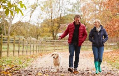 Foto van twee mensen die aan het wandelen zijn met een hond in de herfst